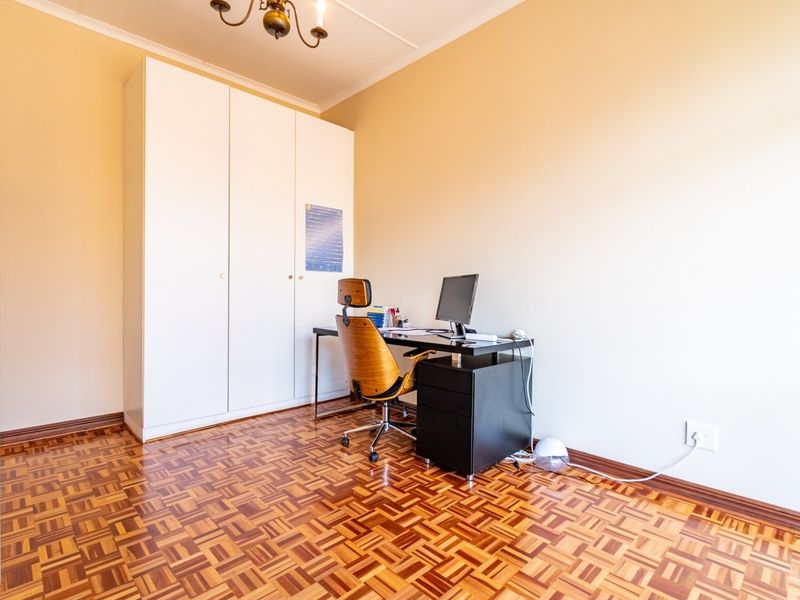 A bedroom featuring classic parquet flooring, a built-in wardrobe, and neutral wall finishes, currently utilized as a home office space.