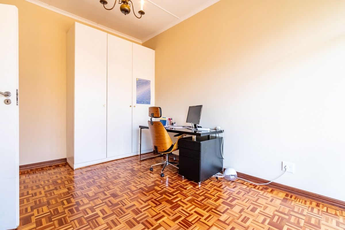 A bedroom featuring classic parquet flooring, a built-in wardrobe, and neutral wall finishes, currently utilized as a home office space.