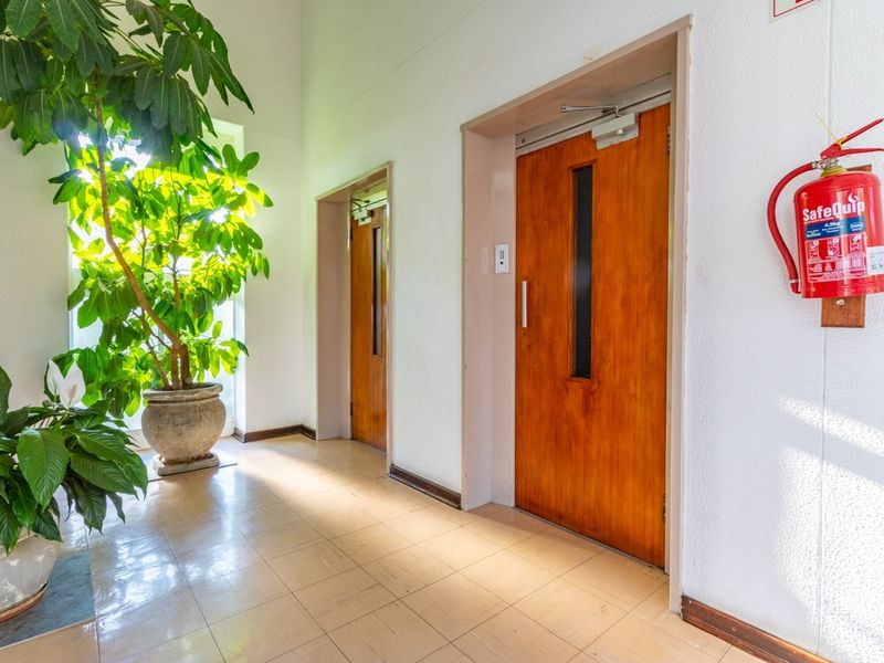 A clean apartment building hallway featuring elevator access, tiled flooring, and a wall-mounted fire extinguisher.