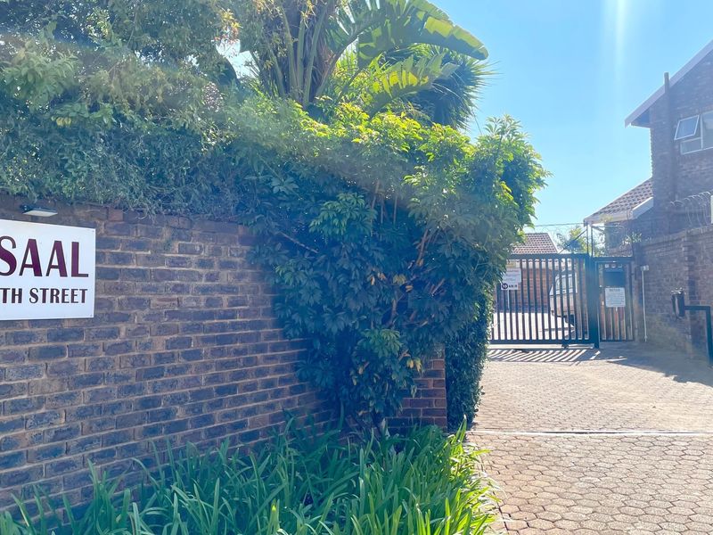 Front entrance view of the Afsaal apartment complex, featuring a brick boundary wall, paved driveway, and secure gated access.