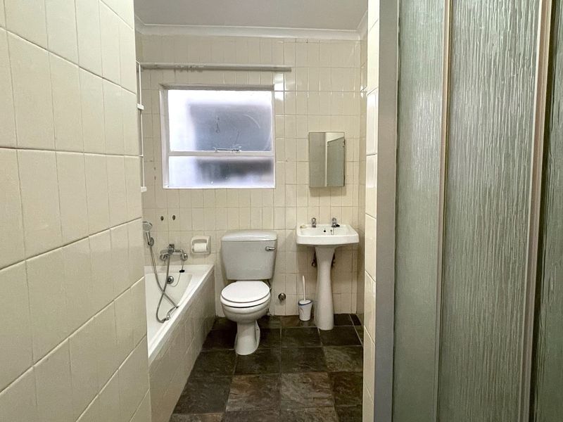 A functional bathroom featuring a pedestal basin, bathtub, and separate shower enclosure with dated ceramic tiling throughout.