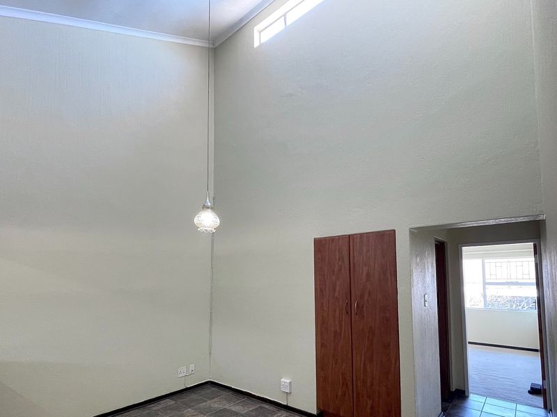 An empty living area featuring high ceilings, a clerestory window, tiled flooring, and a built-in storage cupboard.
