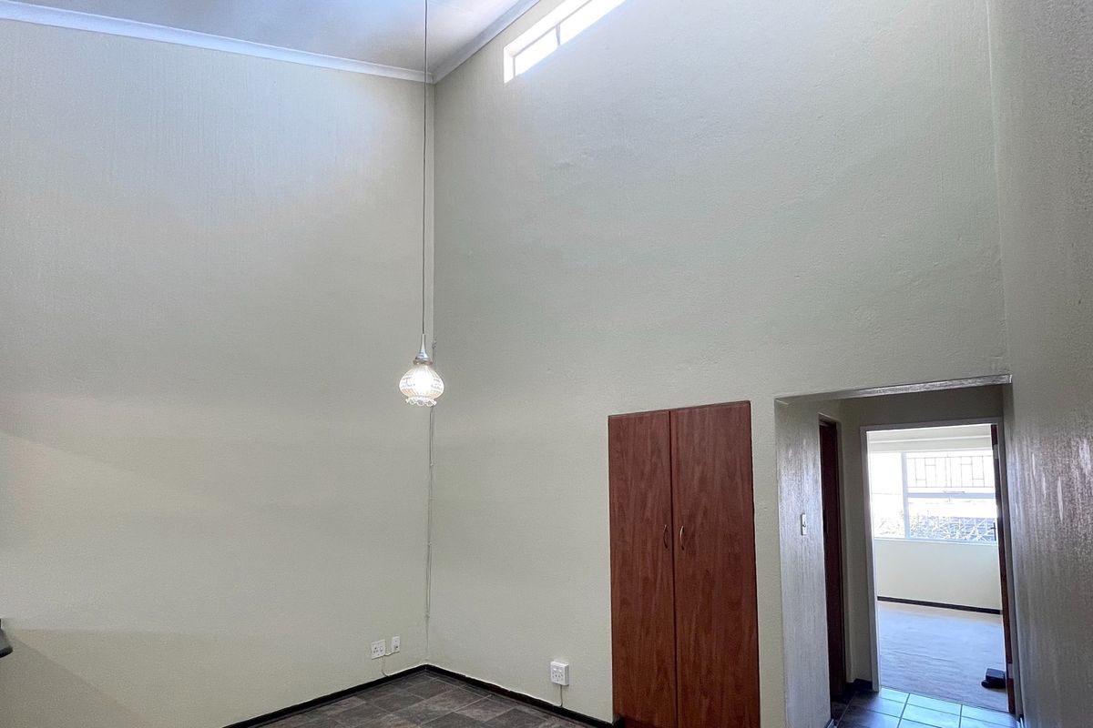 An empty living area featuring high ceilings, a clerestory window, tiled flooring, and a built-in storage cupboard.