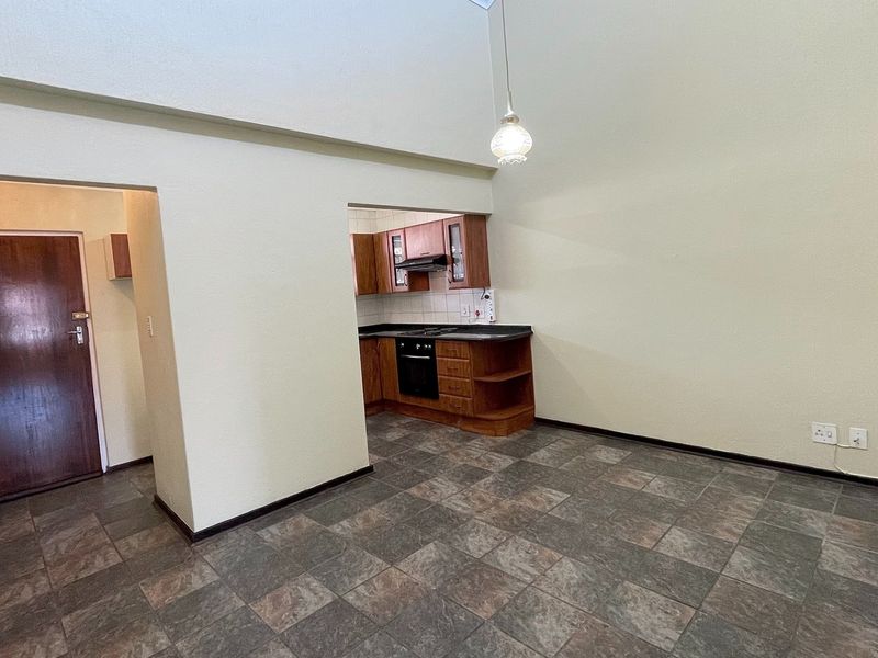 An open-plan living area featuring tiled flooring, high ceilings, and a compact kitchen with built-in cabinetry, oven, and hob.