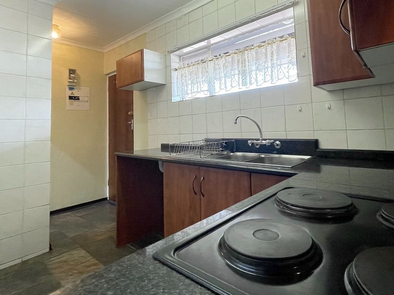 A functional kitchen featuring built-in cabinetry, laminate countertops, a stainless steel sink, and an electric hob with tiled splashbacks.