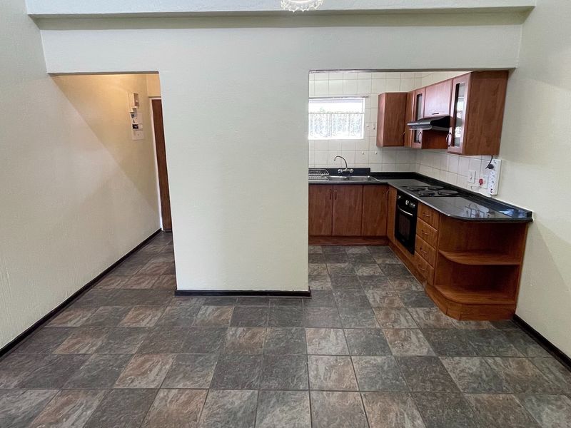 Open plan kitchen area featuring wooden cabinetry, built-in appliances, and tiled flooring, offering a functional layout ready for modern updates.