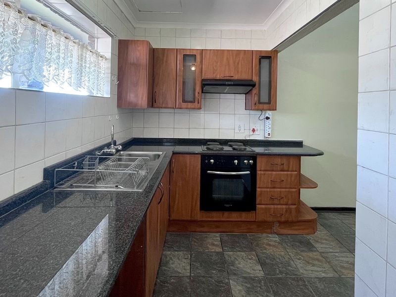 A functional kitchen featuring granite countertops, built-in oven, electric hob, extractor fan, and ample wooden cabinetry with tiled splashbacks.