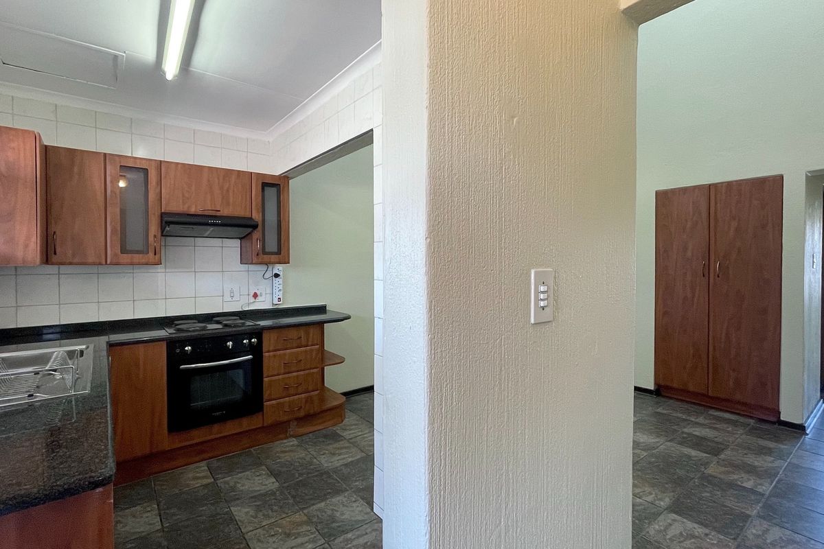 A functional kitchen featuring wooden cabinetry, granite countertops, built-in oven and hob, and tiled flooring, adjacent to a hallway with built-in storage.
