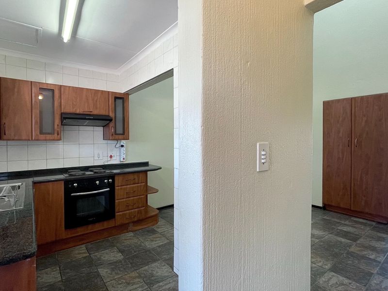 A functional kitchen featuring wooden cabinetry, granite countertops, built-in oven and hob, and tiled flooring, adjacent to a hallway with built-in storage.