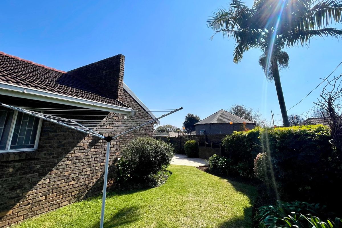 A view of the rear garden featuring a brick exterior, a well-maintained lawn, perimeter hedging, and a rotary clothesline.