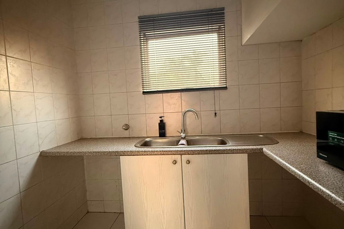 A functional scullery or utility area featuring a stainless steel sink, laminate countertops, and tiled finishes, offering a practical space for laundry or prep.