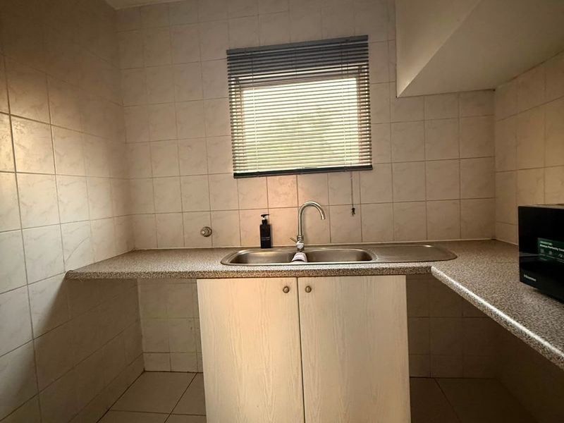 A functional scullery or utility area featuring a stainless steel sink, laminate countertops, and tiled finishes, offering a practical space for laundry or prep.