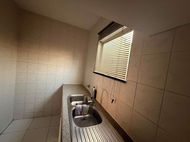 A functional laundry area featuring a stainless steel double sink, tiled walls, and tiled flooring, providing a practical space for utility tasks.