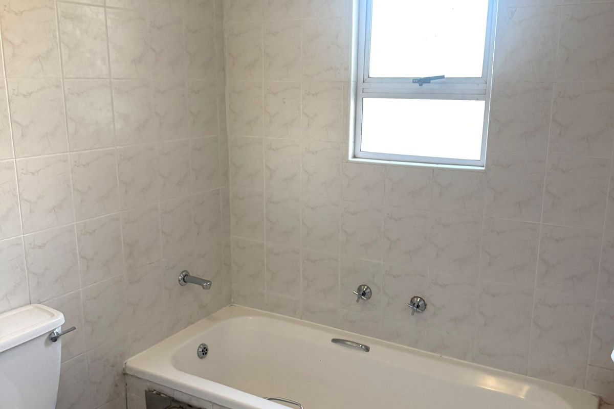 A functional bathroom featuring a bathtub, pedestal basin, and toilet with neutral wall and floor tiling.