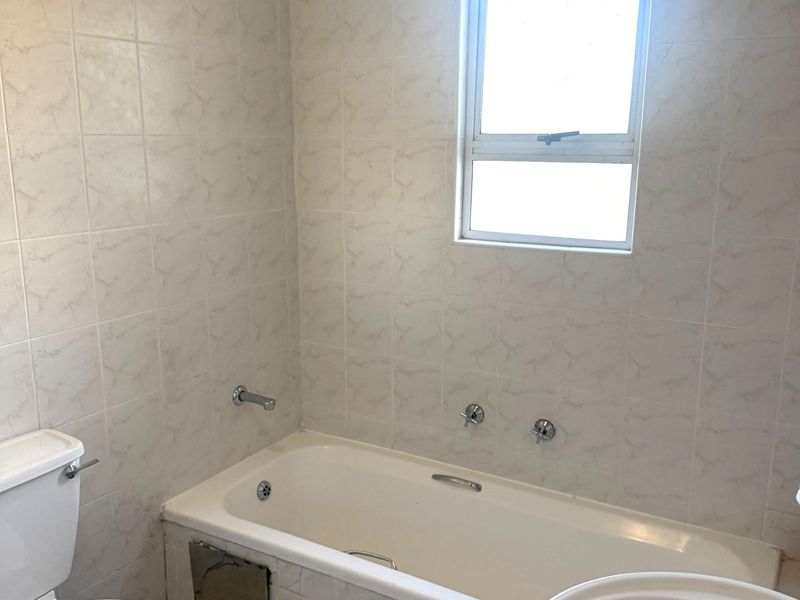 A functional bathroom featuring a bathtub, pedestal basin, and toilet with neutral wall and floor tiling.