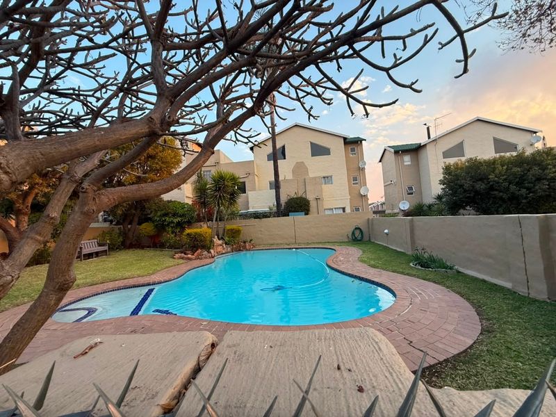 A backyard area featuring a swimming pool with brick coping, surrounded by a lawn and a perimeter boundary wall.