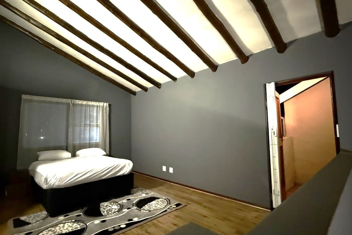 Spacious bedroom featuring a vaulted ceiling with exposed timber beams, laminate flooring, and neutral grey walls, offering a cozy and modern atmosphere.