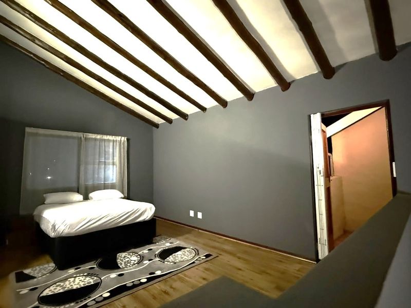 Spacious bedroom featuring a vaulted ceiling with exposed timber beams, laminate flooring, and neutral grey walls, offering a cozy and modern atmosphere.