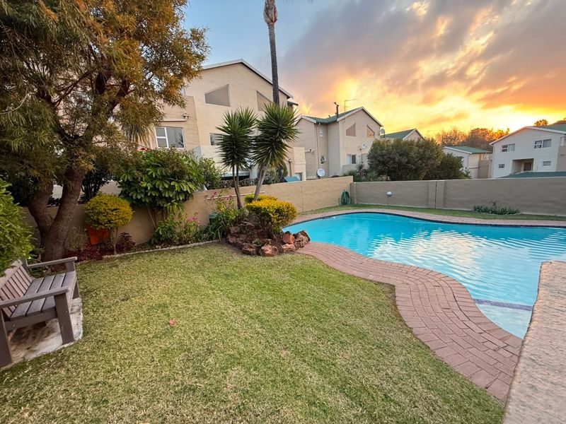 A well-maintained outdoor pool area featuring a swimming pool, brick-paved surround, and established garden landscaping within a secure boundary wall setting.