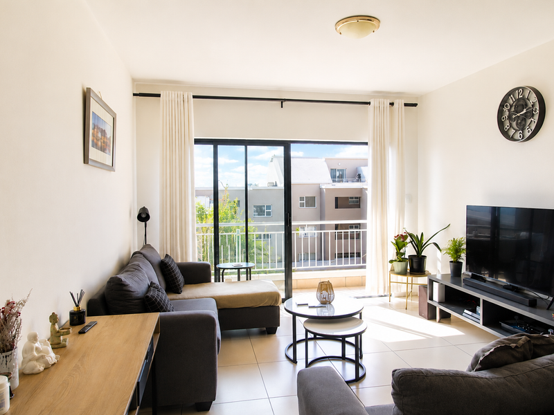 Bright living room featuring tiled flooring and a large sliding glass door providing access to a balcony with natural light.