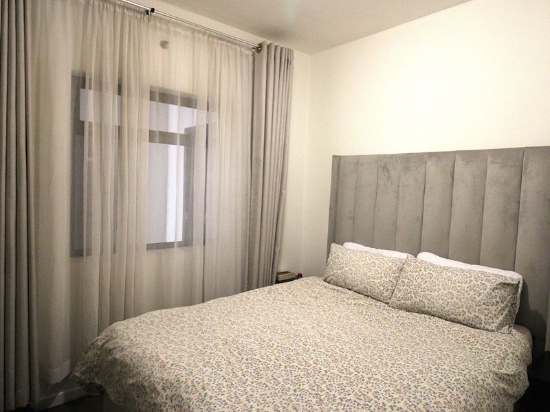A well-maintained bedroom featuring neutral wall finishes and a large window with floor-to-ceiling curtains.