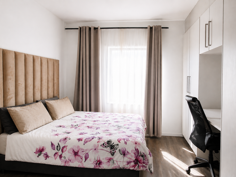A well-lit bedroom featuring built-in cupboards, laminate flooring, and a neutral color palette, creating a comfortable and functional living space.