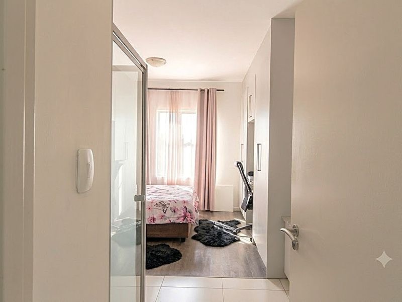 A view from the hallway into a bedroom featuring built-in cupboards, laminate flooring, and an adjacent glass-enclosed shower area.