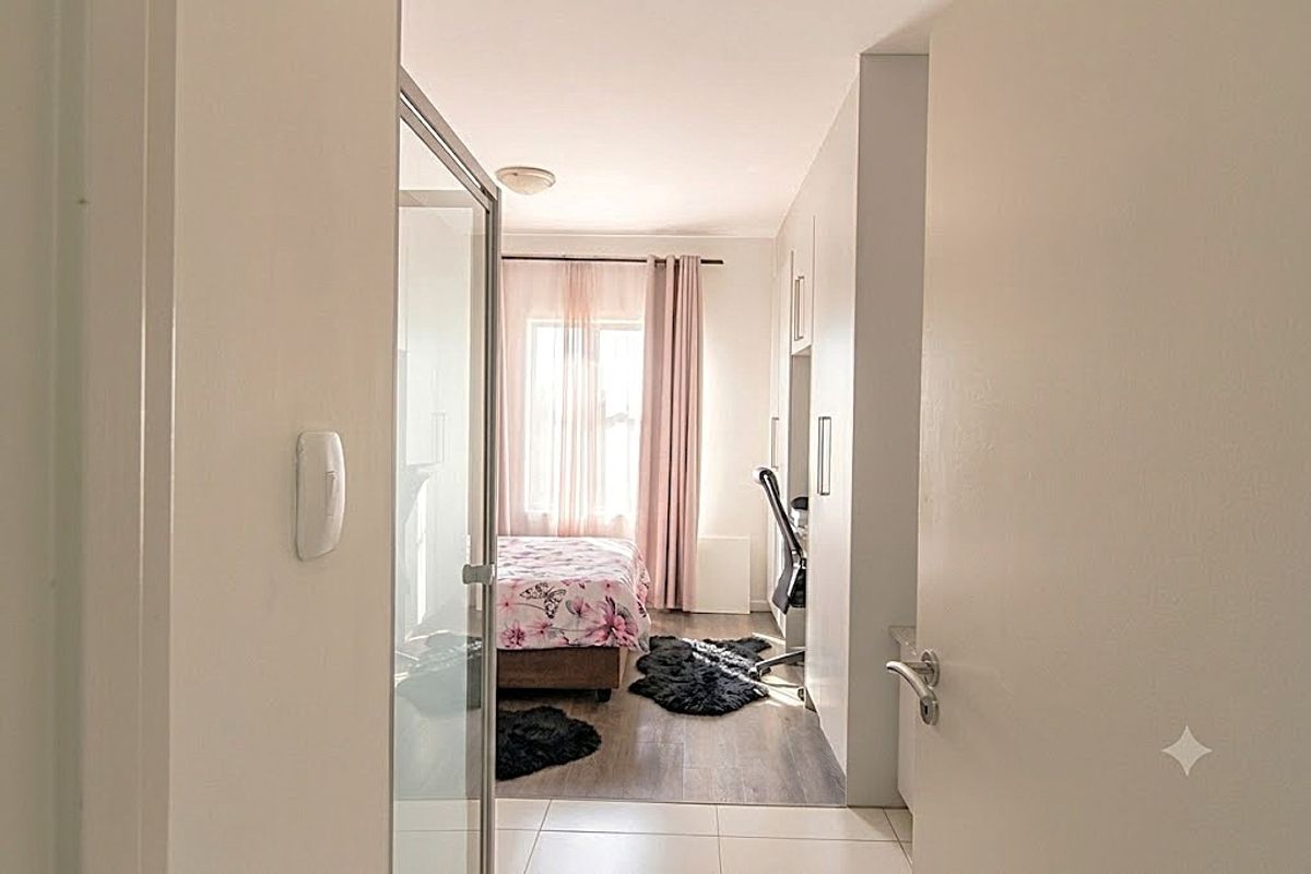 A view from the hallway into a bedroom featuring built-in cupboards, laminate flooring, and an adjacent glass-enclosed shower area.