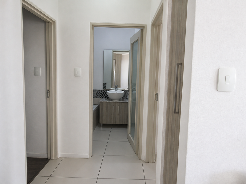 A clean, neutral hallway featuring tiled flooring and access to adjacent rooms, including a view into a bathroom with a vanity basin.