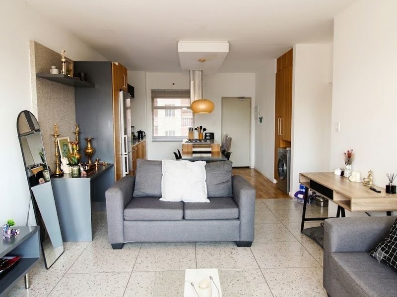 Open-plan living and kitchen area featuring modern cabinetry, integrated laundry space, and neutral terrazzo-style flooring in a well-maintained apartment setting.