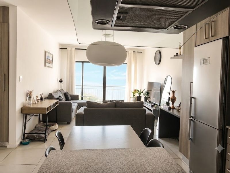 Modern open-plan living area featuring a sleek kitchen with stone countertops, integrated cabinetry, and large sliding doors leading to a balcony with scenic views.