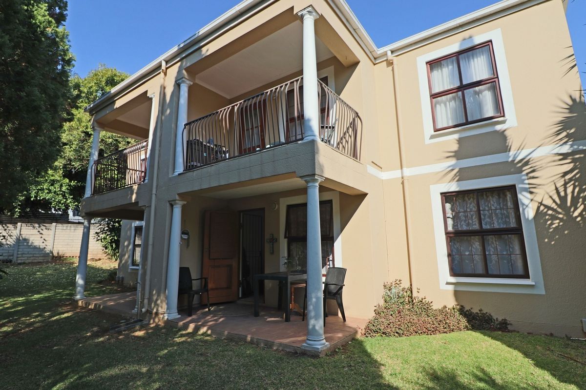 Rear view of a two-story apartment building featuring a ground-floor patio and an upper-level balcony with classic columns and wrought iron railings.