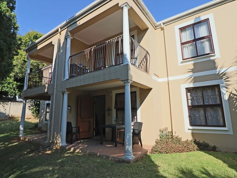 Rear view of a two-story apartment building featuring a ground-floor patio and an upper-level balcony with classic columns and wrought iron railings.