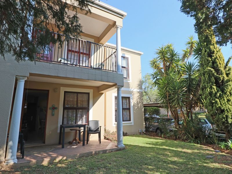 Rear view of the apartment building featuring a ground floor patio and an upper level balcony with metal railings and structural columns.