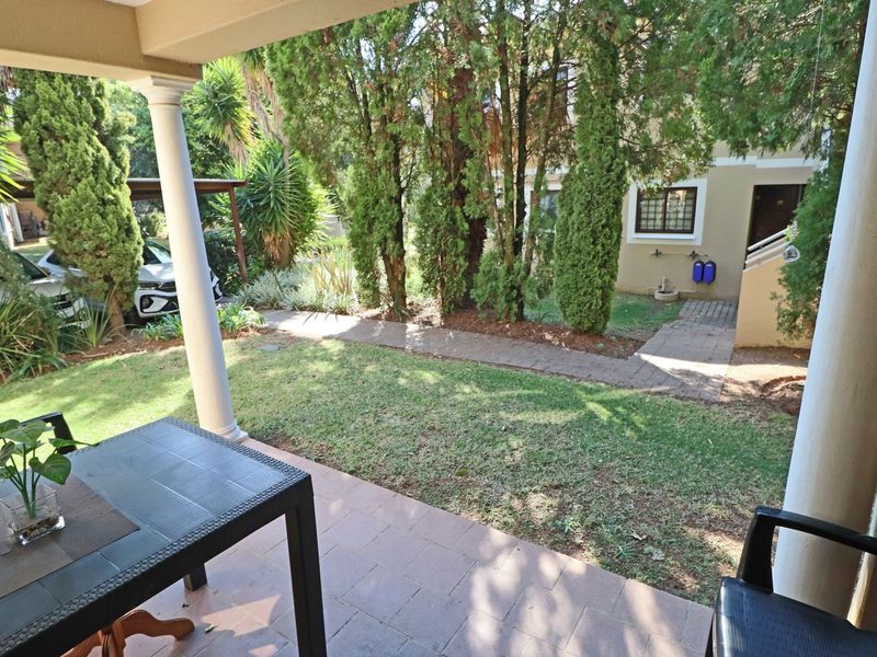 A covered patio overlooking a private garden area with a paved walkway and established trees.