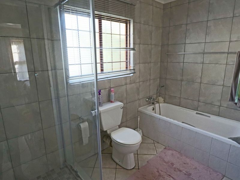 A functional bathroom featuring a glass shower enclosure, a built-in bathtub, and neutral ceramic tiling throughout.