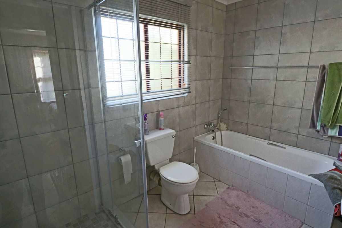 A functional bathroom featuring a glass shower enclosure, a built-in bathtub, and neutral ceramic tiling throughout.