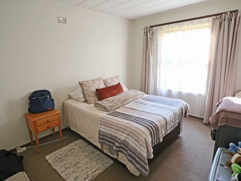 A standard bedroom featuring neutral wall finishes, carpeted flooring, and a window with installed curtain rods.