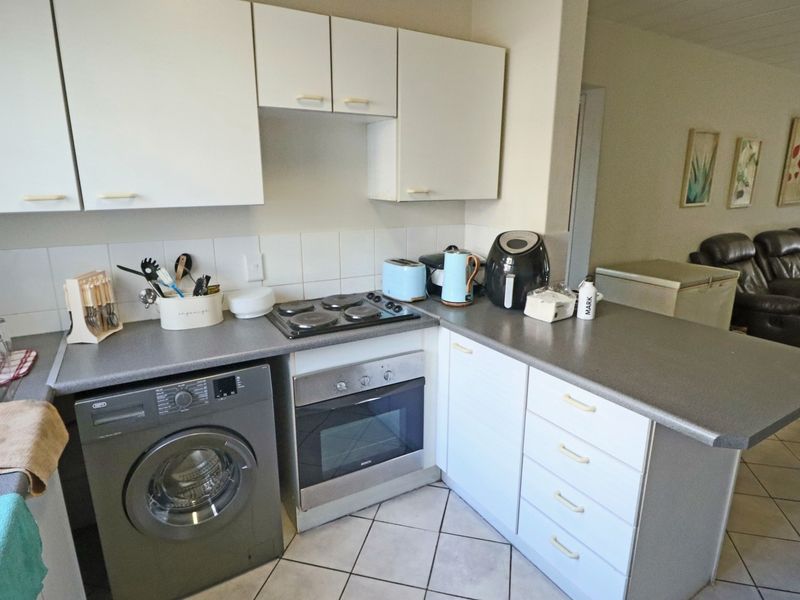 Compact kitchen featuring white cabinetry, laminate countertops, built-in oven, electric hob, and tiled flooring, offering a functional layout for daily meal preparation.