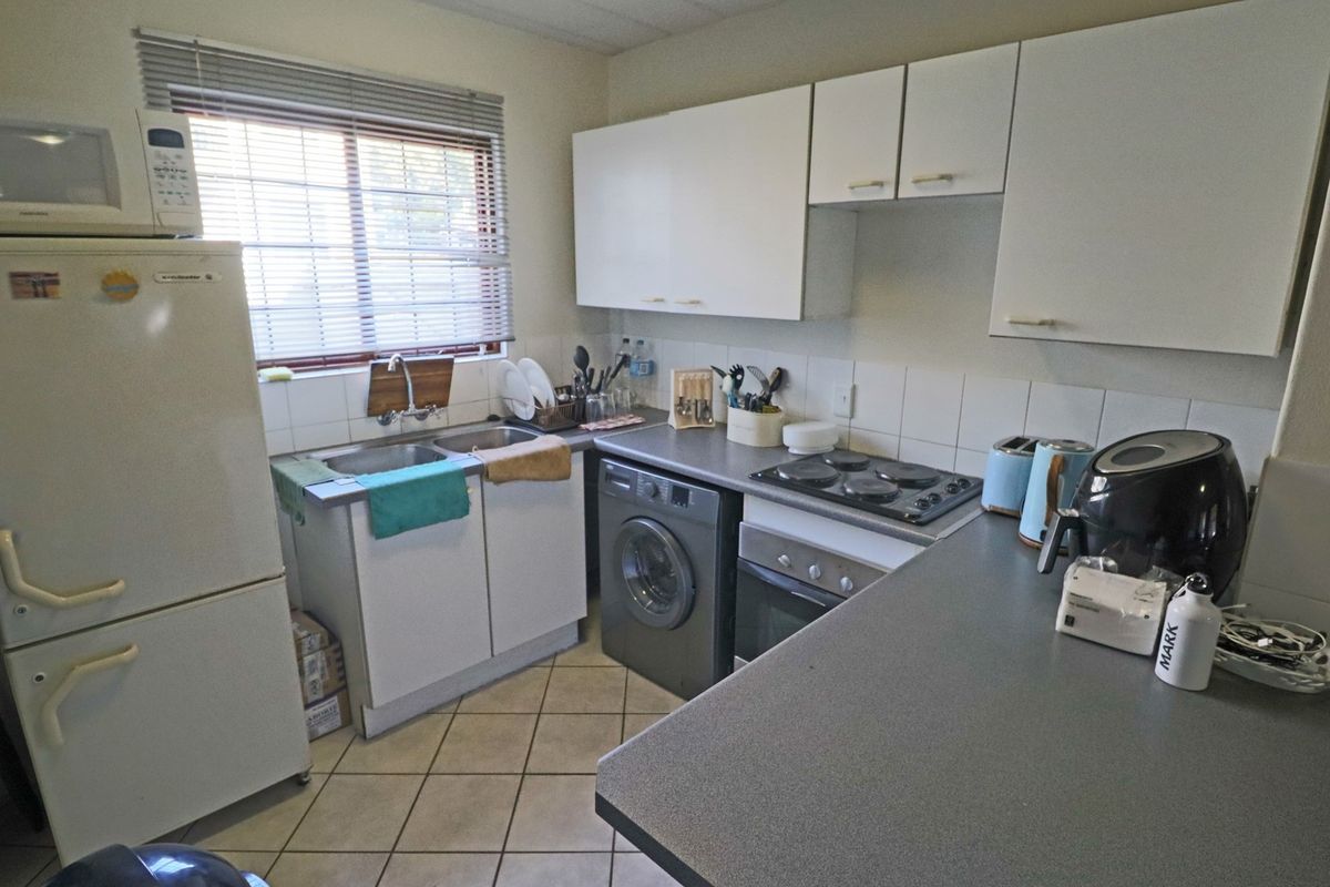 A functional kitchen featuring white cabinetry, tiled splashbacks, a double basin sink, and built-in cooking appliances with tiled flooring.