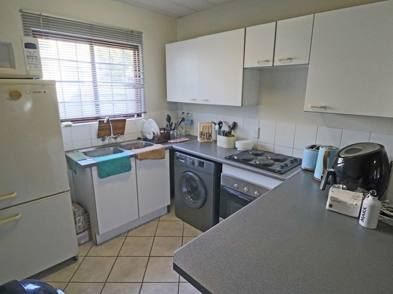 A functional kitchen featuring white cabinetry, tiled splashbacks, a double basin sink, and built-in cooking appliances with tiled flooring.