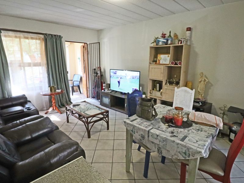 Open-plan living and dining area featuring tiled flooring and access to an outdoor space through a sliding door with a security gate.
