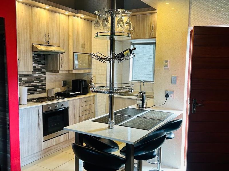 Modern kitchen featuring light wood cabinetry, stone countertops, a central breakfast bar with integrated shelving, and high-quality built-in appliances under a vaulted ceiling.