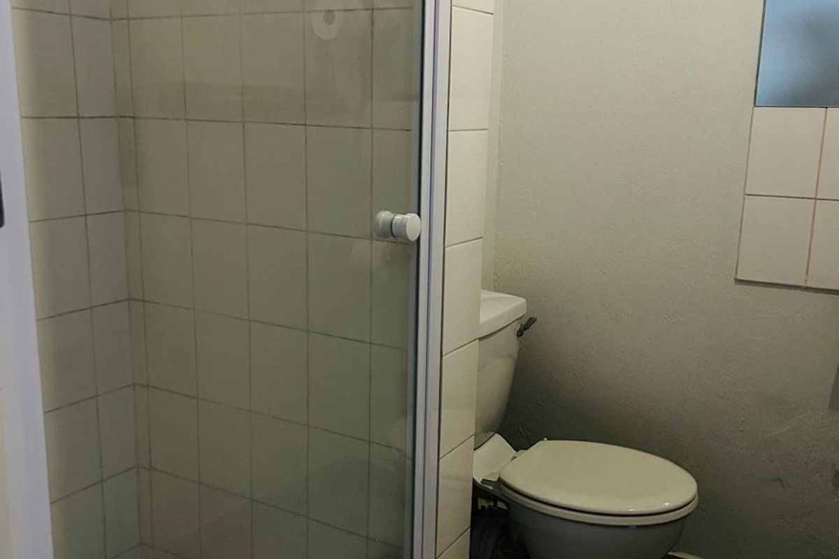 A compact bathroom featuring a shower enclosure, toilet, and tiled finishes. The space is functional but would benefit from cosmetic updates.