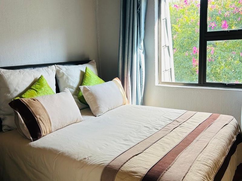 A cozy bedroom featuring exposed timber ceiling beams, a wall-mounted air conditioning unit, and a window overlooking greenery.