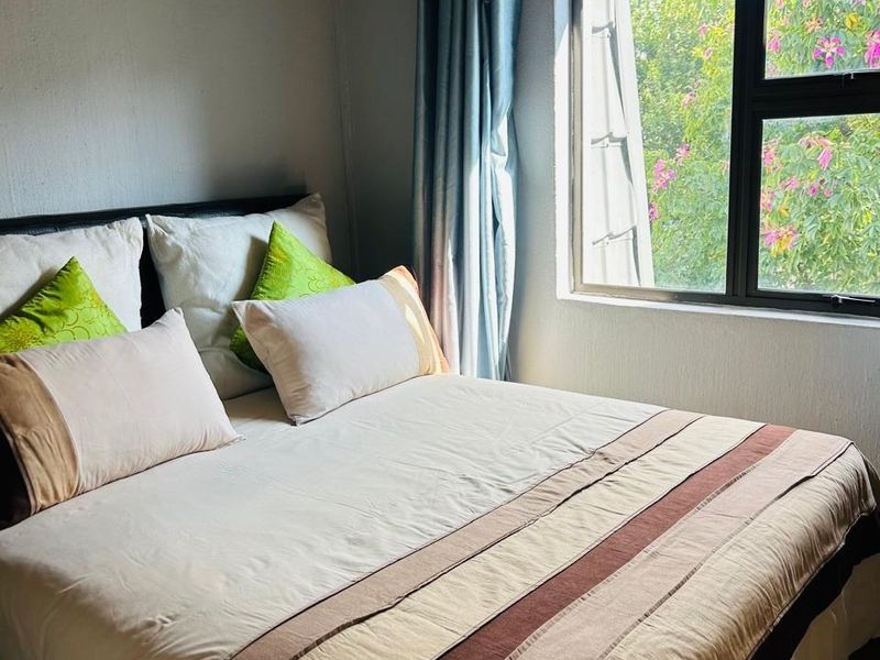 A cozy bedroom featuring exposed timber rafters and a large window with views of greenery.