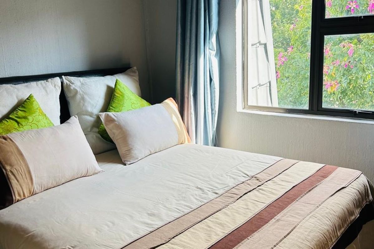 A cozy bedroom featuring exposed timber rafters and a large window with views of greenery.