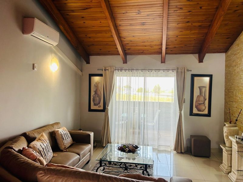 Spacious living room featuring a high exposed timber beam ceiling, tiled flooring, split-system air conditioning, and a stone feature wall with balcony access.