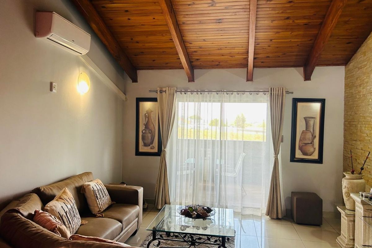 Spacious living room featuring a high exposed timber beam ceiling, tiled flooring, split-system air conditioning, and a stone feature wall with balcony access.