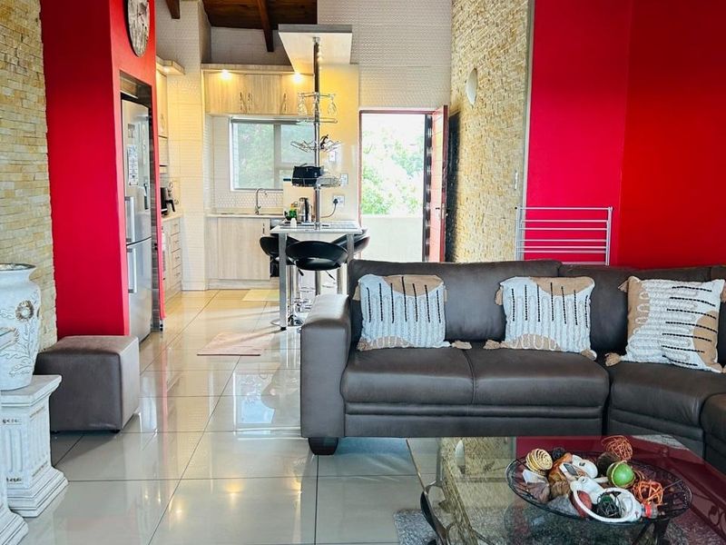 Open-plan living and kitchen area featuring high exposed timber ceilings, stone feature walls, and polished floor tiles with a modern kitchen layout.